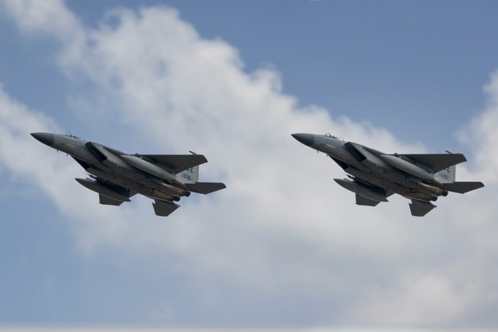 two fighter jets flying in the sky with a cloud in the background